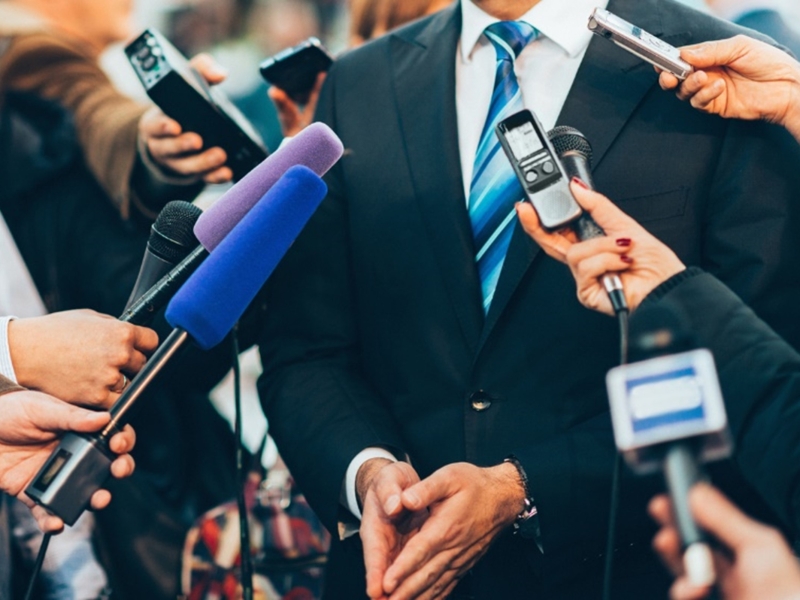 a man in a suit from neck down with microphones and people around him