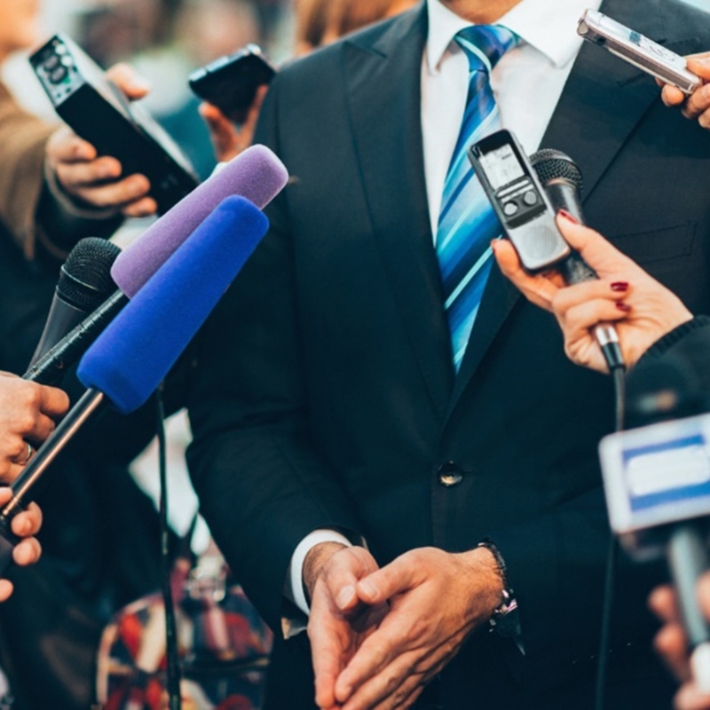 a man in a suit from neck down with microphones and people around him