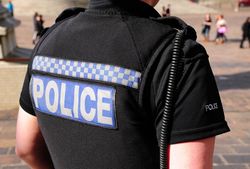 Back of a black police uniform with Blue and white "police" text. and wire hanging down the back