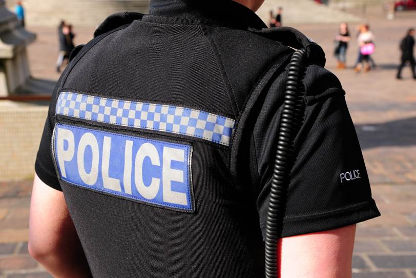 Back of a black police uniform with Blue and white "police" text. and wire hanging down the back